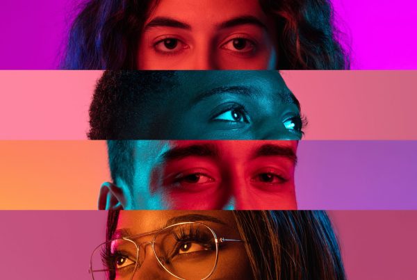 Close-up de quatro pares de olhos, cada um pertencendo a diferentes indivíduos, dispostos horizontalmente com fundos vibrantes e multicoloridos. Esta imagem representa a diversidade e inclusão, destacando várias etnias e géneros. As cores vivas e o foco nos olhos enfatizam as perspetivas únicas e a importância da representatividade.