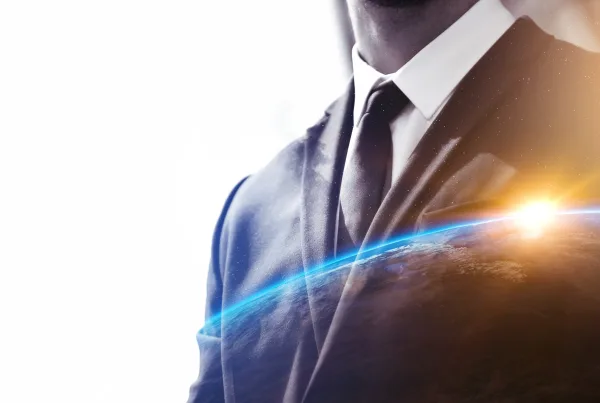 Imagem conceptual de um homem de fato e gravata, com um efeito de dupla exposição mostrando o horizonte da Terra ao fundo, simbolizando a conexão entre negócios e tecnologia global. A luz do sol ao fundo realça a inovação e o crescimento no ambiente empresarial.
